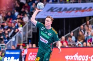 Ein männlicher Handballspieler im grünen Trikot der TSV Hannover-Burgdorf bereitet sich während eines Spiels der Handball-Bundesliga auf den Wurf vor, während die Zuschauer von der Tribüne aus zuschauen - Teil der THW Kiel Saison 2025/2026.
