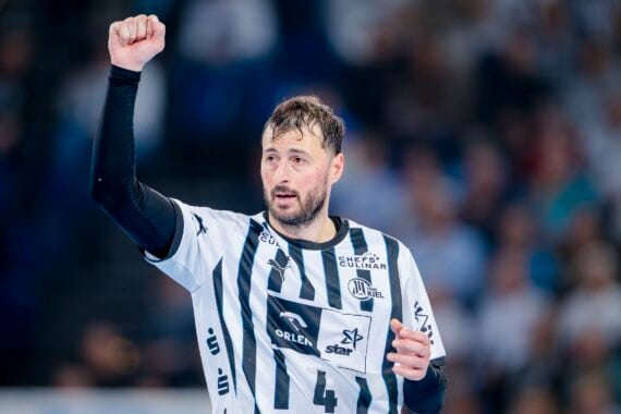 Ein männlicher Handballspieler in einem weiß-schwarz gestreiften Trikot des THW Kiel reckt während eines Spiels der Handball-Bundesliga die rechte Faust in die Luft, im Hintergrund sind Zuschauer zu sehen.