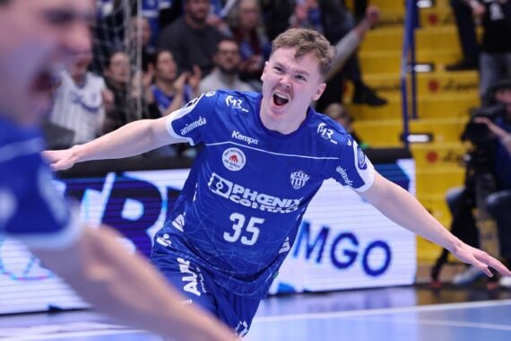 Ein männlicher Handballspieler im blauen Trikot mit der Nummer 35 jubelt energisch mit weit ausgebreiteten Armen auf einem Hallenplatz, während Fans und Fotografen im Hintergrund zuschauen.