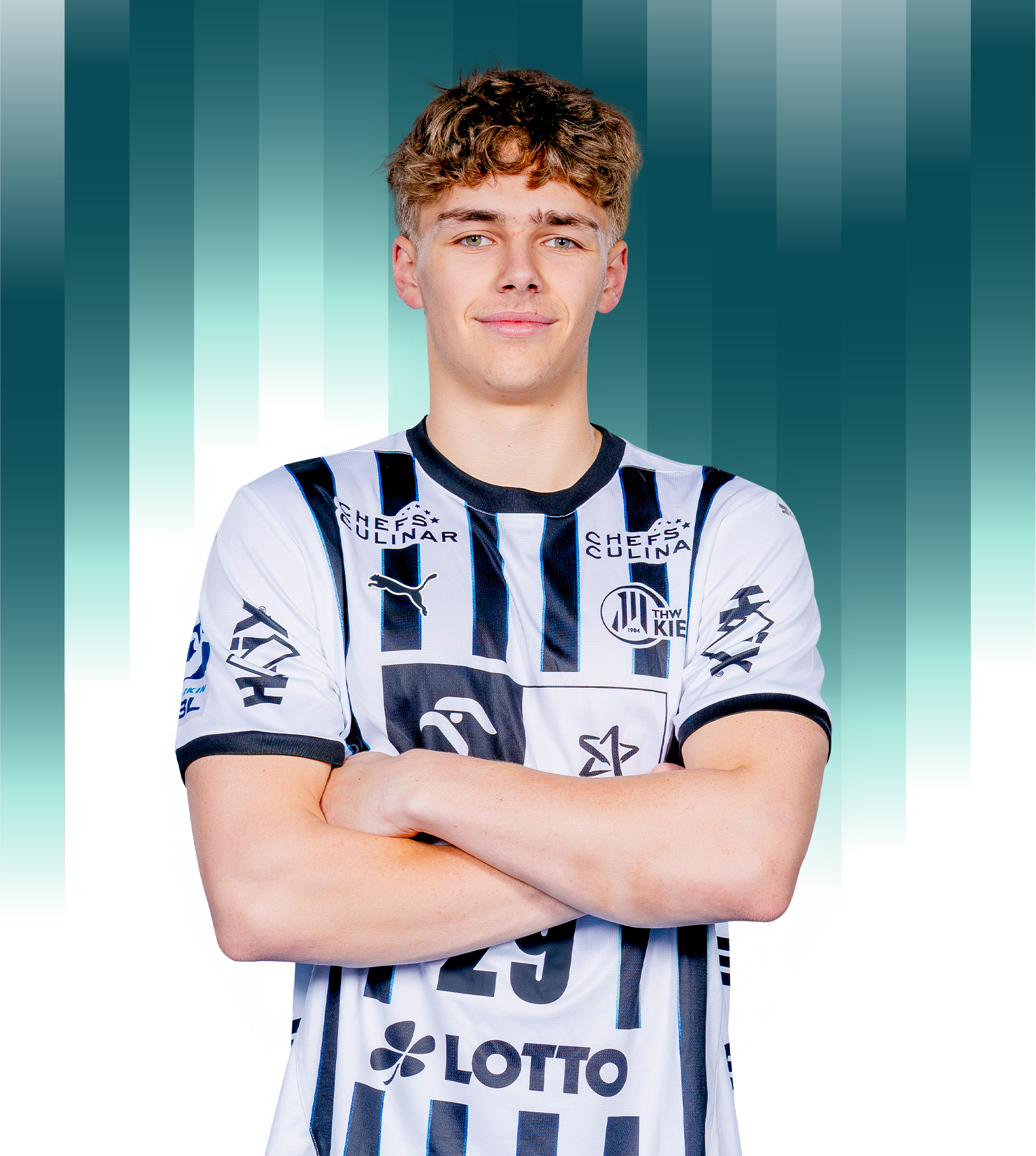 Ein junger männlicher Fußballspieler mit kurzen lockigen Haaren steht selbstbewusst mit verschränkten Armen da und trägt ein weiß-schwarz gestreiftes Trikot mit Logos vor einem blaugrünen und weißen Hintergrund mit Farbverlauf.
