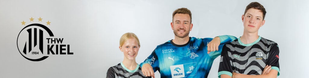 Drei Personen in Trikots des THW Kiel stehen nebeneinander, posieren und lächeln vor einem weißen Hintergrund mit dem Logo des THW Kiel und den Sternen auf der linken Seite.