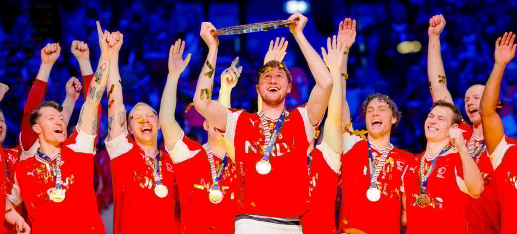 Ein jubelndes Männerhandballteam in roten Trikots, mit Medaillen um den Hals, feiert, während ein Spieler inmitten von Konfetti und jubelnden Mannschaftskameraden eine Trophäe über seinen Kopf hebt.