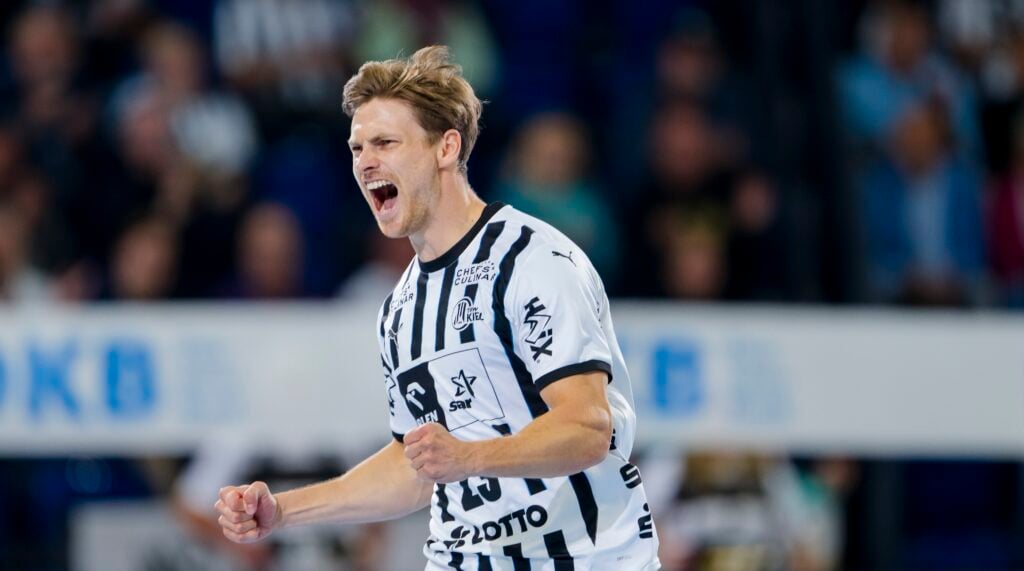 HANDBALL 2025/26: THW Kiel - GWD Minden Ein männlicher Handballspieler in einem schwarz-weiß gestreiften Trikot feiert leidenschaftlich mit geballten Fäusten und offenem Mund, möglicherweise schreiend, während eines Spiels in einer Halle.