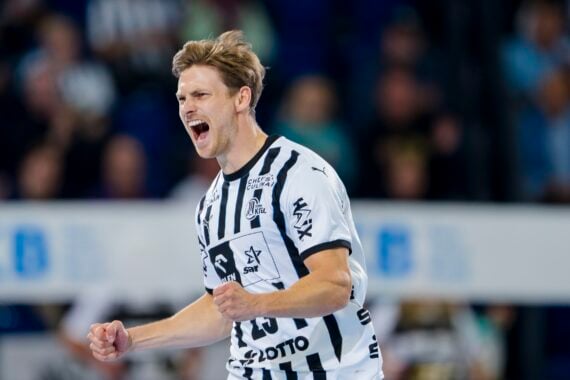 Ein männlicher Handballspieler in einem schwarz-weiß gestreiften Trikot feiert leidenschaftlich mit geballten Fäusten und offenem Mund, möglicherweise schreiend, während eines Spiels in einer Halle.