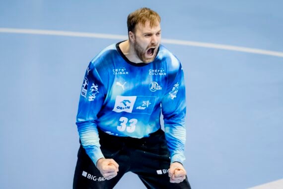 Ein männlicher Handballtorwart in einem blauen Trikot mit der Nummer 33 ballt die Fäuste und jubelt auf einem hellblauen Hallenplatz.