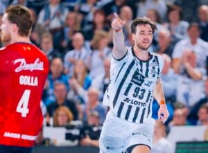 Ein männlicher Handballspieler in einem weiß-schwarz gestreiften Trikot mit der Nummer 93 zeigt nach vorne und jubelt. Ein anderer Spieler in einem roten Trikot, Nummer 4, steht im Vordergrund. Im Hintergrund ist eine jubelnde Menge zu sehen.