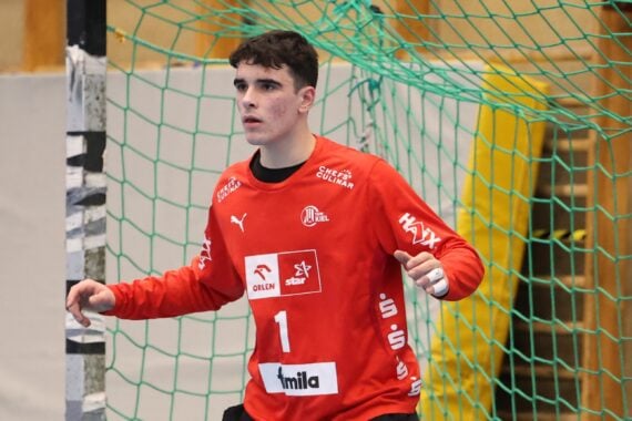 Ein männlicher Handballtorwart in einem roten Trikot mit der Nummer 1, der den THW Kiel Handball-Bundesliga Saison 2025/2026 repräsentiert, steht wachsam vor dem Tor, bereit, einen Schuss zu blocken. Im Hintergrund sind ein grünes Netz und eine Sporthalle zu sehen.