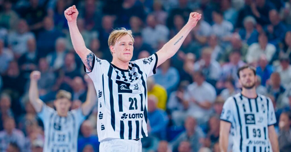Ein Handballspieler des THW Kiel im schwarz-weiß gestreiften Trikot reißt während der Handball-Bundesliga Saison 2025/2026 beide Arme jubelnd in die Höhe. Im Hintergrund sind zwei Mitspieler und eine unscharfe Menschenmenge zu sehen.