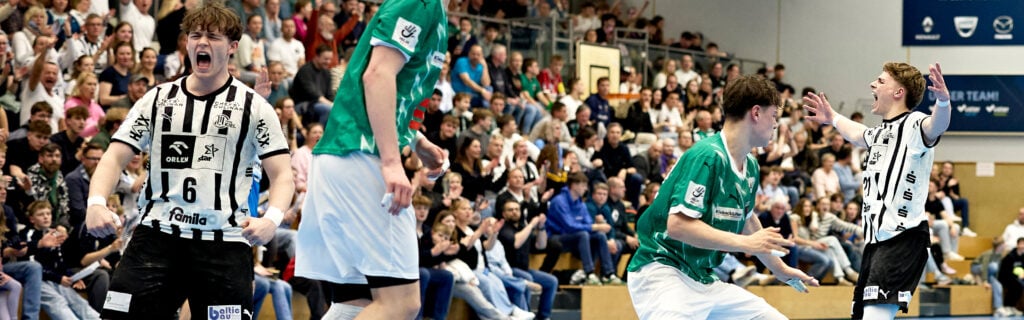 Hallenhandballspiel: Die U19-Spieler des THW Kiel und des SC Magdeburg feiern während des Finales der Deutschen Meisterschaft ausgelassen auf dem Spielfeld, während die Zuschauer im Hintergrund von der Tribüne aus zusehen.