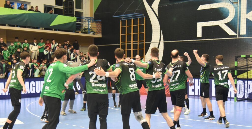 Eine Gruppe männlicher Handballspieler in grün-schwarzen Trikots feiert auf einem Hallenplatz vor jubelnden Fans auf der Tribüne. Die Stimmung ist ausgelassen, und die Mannschaft scheint ein Spiel gewonnen zu haben.