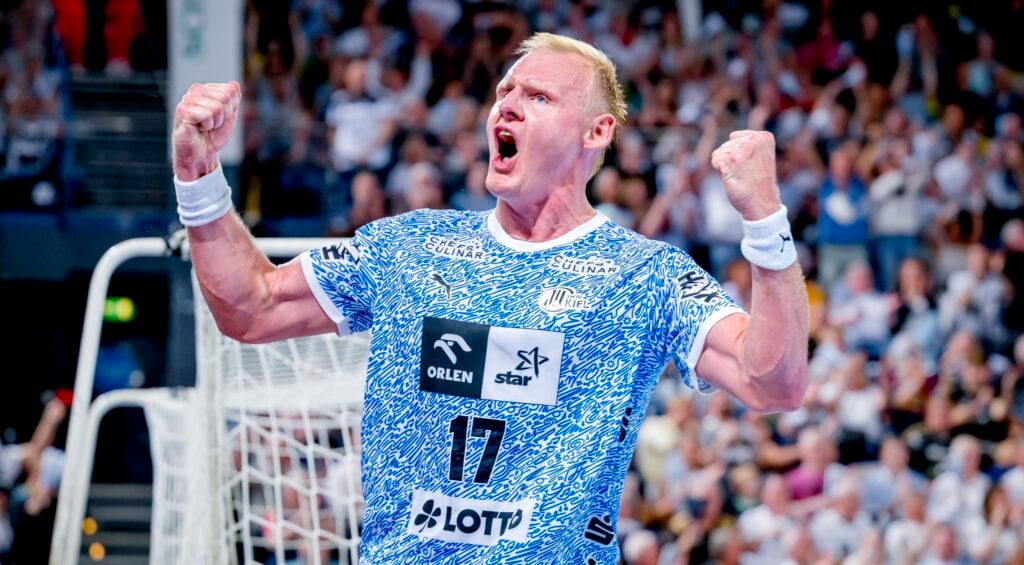 Ein Handballspieler in einem blau-weißen Trikot mit der Nummer 17 feiert leidenschaftlich mit geballten Fäusten und offenem Mund vor einer jubelnden Menge.