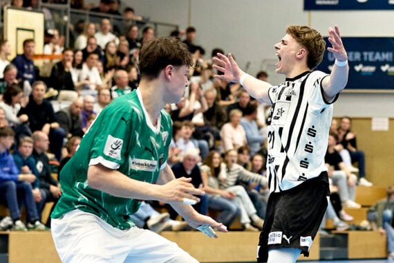 Ein U19-Handball-Bundesligaspieler des THW Kiel im schwarz-weißen Trikot jubelt mit ausgebreiteten Armen, während ein Jugendspieler des SC Magdeburg in Grün vor dem jubelnden Publikum beim Finale der Deutschen Meisterschaft reagiert.