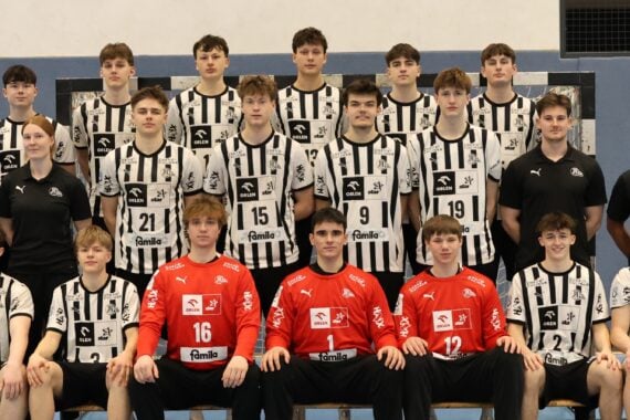Ein Gruppenfoto einer Jugendhandballmannschaft in schwarz-weiß gestreiften Trikots mit vier Trainern in schwarzen Hemden. Die Spieler stehen und sitzen in Reihen auf einer Bank in einer Sporthalle.