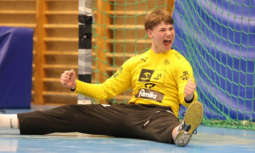 Ein junger männlicher THW-Torwart im gelben Trikot sitzt nach dem 36:36-Finale der Handball-Bundesliga Jugend Deutsche Meisterschaft 2025/2026 gegen die Füchse mit erhobenen Armen und offenem Mund jubelnd auf dem Boden vor dem Tor.
