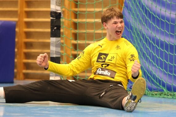 Ein junger männlicher THW-Torwart im gelben Trikot sitzt nach dem 36:36-Finale der Handball-Bundesliga Jugend Deutsche Meisterschaft 2025/2026 gegen die Füchse mit erhobenen Armen und offenem Mund jubelnd auf dem Boden vor dem Tor.