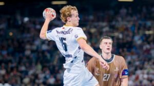 Ein männlicher Handballspieler des THW Kiel im weißen Trikot springt zum Wurf, während ein Abwehrspieler im braunen Trikot ihn während der Handball-Bundesliga Saison 2025/2026 blockiert. Fans beobachten, wie sich Petter Överby auf seinen emotionalen Abschied vorbereitet.