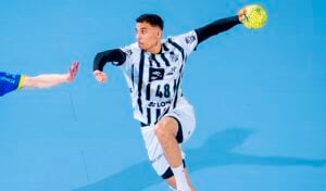 THW Kiels Petter Överby, im weiß-schwarz gestreiften Trikot, springt während der Handball-Bundesliga Saison 2025/2026 zum Wurf eines gelben Balls, während ein Gegenspieler in Blau die Hand ausstreckt - ein spannender Moment vor Överbys Abschied.