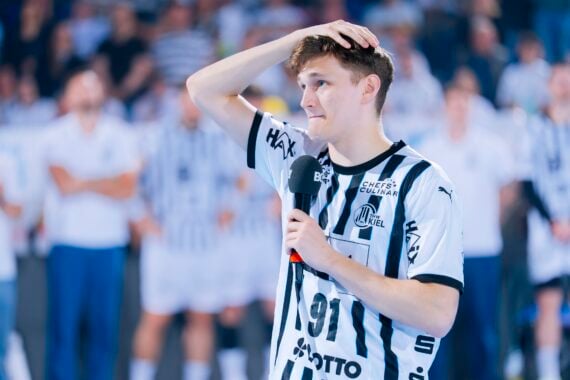 Ein junger männlicher Handballspieler in einem schwarz-weiß gestreiften Trikot, möglicherweise vom THW Kiel, steht auf dem Spielfeld, hält ein Mikrofon in der Hand und schaut nachdenklich - vielleicht zum Abschied von Petter Överby während der Handball-Bundesliga Saison 2025/2026.