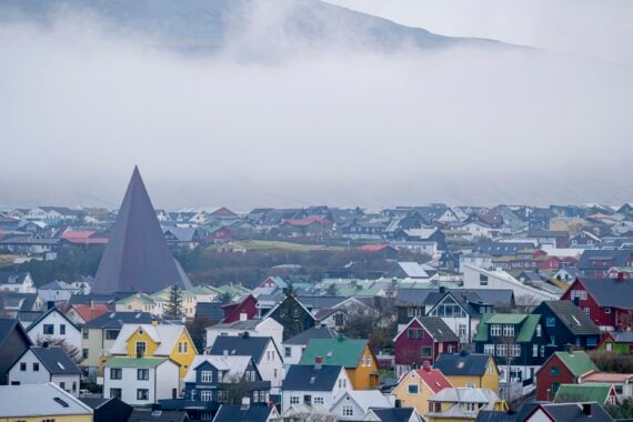 Unter einem nebligen, bewölkten Himmel liegt eine Stadt mit bunten Häusern und Dächern, deren spitzes, dreieckiges Gebäude und Hügel teilweise vom Nebel verdeckt sind – ganz wie Szenen von den Färöern, die sich auf den Wenzel Nordic Cup vorbereiten.