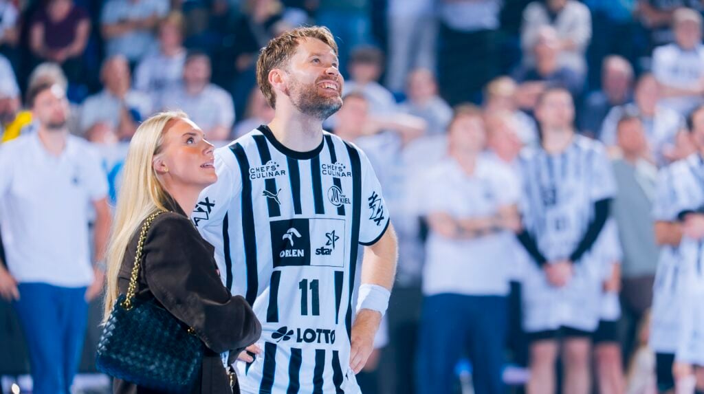 HANDBALL 2025/26: THW Kiel - TBV Lemgo Lippe Ein Handballspieler in einem schwarz-weiß gestreiften Trikot, möglicherweise vom THW Kiel, steht neben einer Frau mit langen blonden Haaren. Beide lächeln und schauen inmitten einer Menschenmenge während der Handball-Bundesliga Saison 2025/2026 und Petter Överby's Abschied auf.