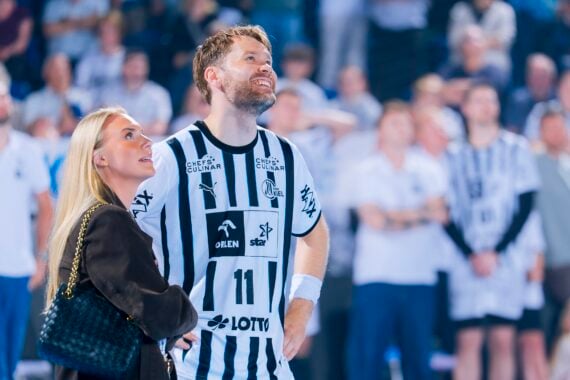 Ein Handballspieler in einem schwarz-weiß gestreiften Trikot, möglicherweise vom THW Kiel, steht neben einer Frau mit langen blonden Haaren. Beide lächeln und schauen inmitten einer Menschenmenge während der Handball-Bundesliga Saison 2025/2026 und Petter Överby's Abschied auf.
