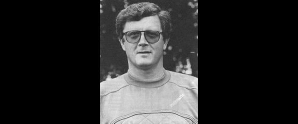 josipmilkovic Schwarz-Weiß-Foto eines Mannes, der eine Brille und ein legeres, langärmeliges Hemd trägt. Er hat kurzes, gewelltes Haar und blickt direkt in die Kamera. Im Hintergrund sind Bäume und unscharfes Laub zu sehen.