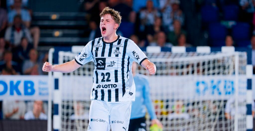 HANDBALL 2025/26: THW Kiel - TBV Lemgo Lippe Ein Handballspieler in einem schwarz-weiß gestreiften Trikot mit der Nummer 22 jubelt mit geballten Fäusten und offenem Mund auf einem Hallenplatz, im Hintergrund sind ein Tor und eine verschwommene Zuschauermenge zu sehen.