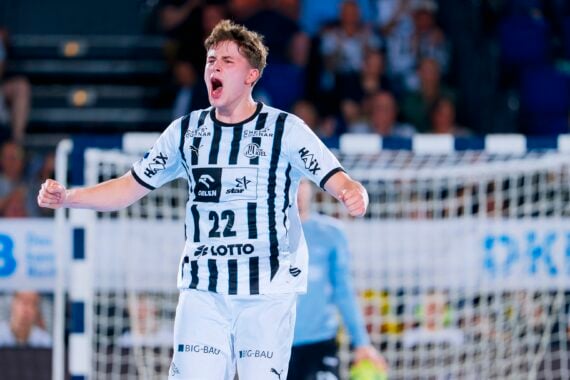Ein Handballspieler in einem schwarz-weiß gestreiften Trikot mit der Nummer 22 jubelt mit geballten Fäusten und offenem Mund auf einem Hallenplatz, im Hintergrund sind ein Tor und eine verschwommene Zuschauermenge zu sehen.