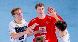 Zwei männliche Handballspieler in weißen Trikots und einer in einem roten Trikot feiern gemeinsam auf dem Spielfeld und klatschen sich nach dem Spiel ab, während im Vordergrund ein weiterer Spieler teilweise zu sehen ist.