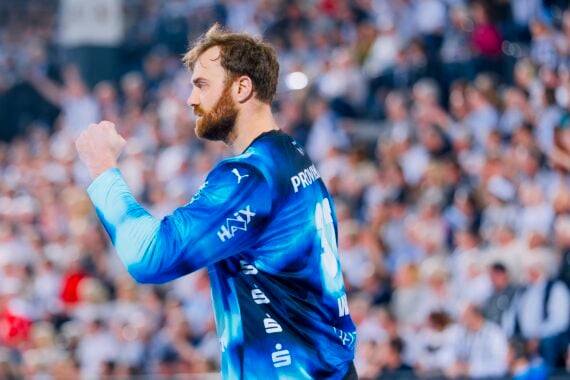 Ein Handballspieler in einem blauen Trikot reckt jubelnd die Faust in die Höhe, im Hintergrund ist eine verschwommene Menschenmenge zu sehen.