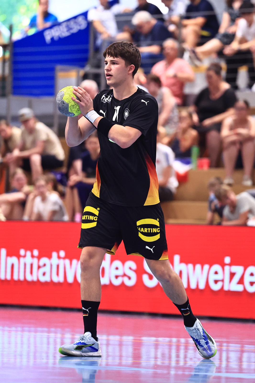 Ein Handballspieler in einem schwarz-gelben Trikot hält den Ball und bereitet sich während eines Spiels in der Handball-Bundesliga-Saison 2026/2027 des THW Kiel auf einen Wurf vor. Im Hintergrund sitzen Zuschauer, die gebannt zusehen, wie Trainer Börge Lund seine Mannschaft mit neuer Strategie und Energie anführt.