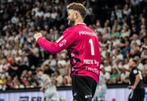 Ein Handballspieler in einem leuchtend pinkfarbenen Trikot mit der Nummer 1 jubelt während eines Spiels, im Hintergrund eine jubelnde Menge.