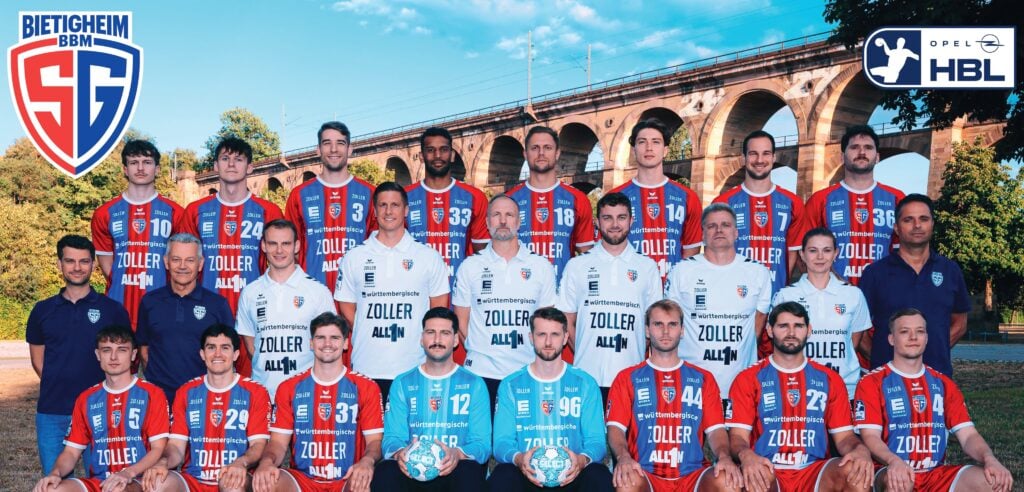 Eine Herren-Handballmannschaft in roten, blauen und weißen Trikots posiert im Freien vor einer großen Steinbrücke. Trainer und Betreuer stehen neben ihnen. In den oberen Ecken sind die Mannschaftslogos zu sehen.