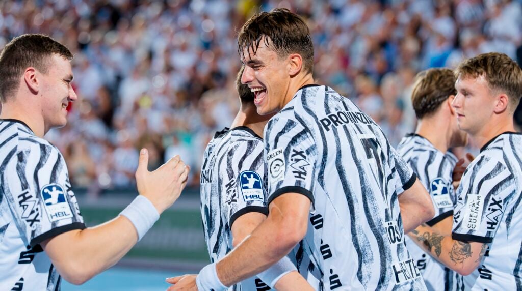 HANDBALL 2026/27: THW Kiel - TBV Lemgo Lippe Eine Gruppe männlicher Handballspieler in schwarz-weißen Trikots lächelt und feiert gemeinsam auf dem Spielfeld, während im Hintergrund eine jubelnde Menschenmenge zu sehen ist.