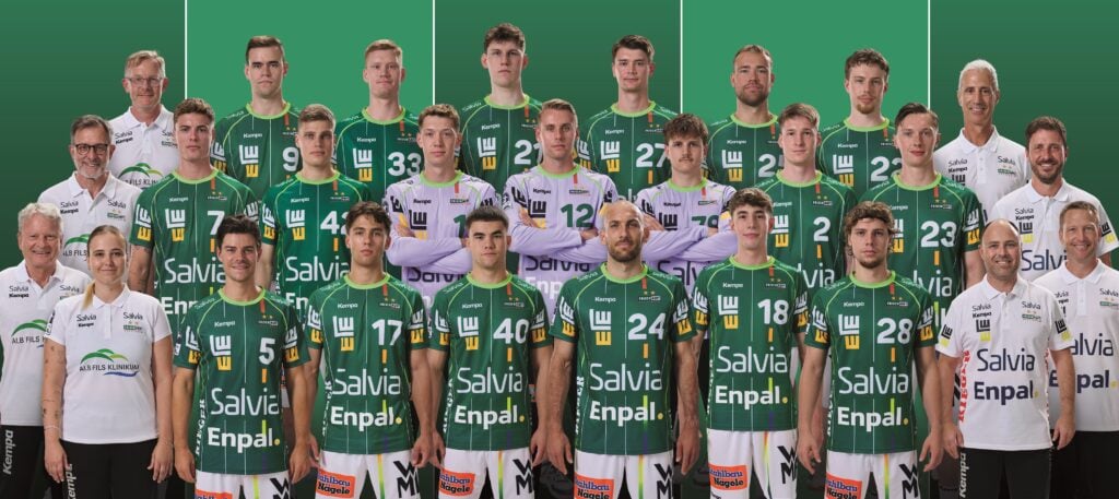 Eine Herren-Volleyballmannschaft in grünen Trikots steht in Reihen zusammen mit Trainern und Betreuern und posiert gemeinsam vor einem grünen Hintergrund.