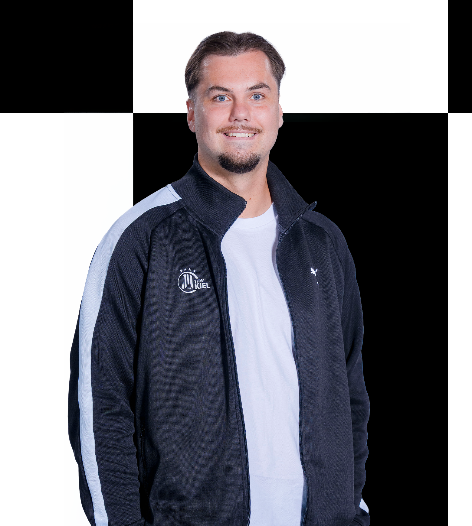 Niklas Ein Mann mit kurzen Haaren und einem Ziegenbart lächelt in die Kamera. Er trägt ein schwarz-weißes Sakko über einem weißen Hemd und steht vor einem schwarz-weiß karierten Hintergrund – ein Look, der an den Teamstil des THW Kiel erinnert. Als Ansprechpartner für Sponsoren und Partner repräsentiert er die Zusammenarbeit des Vereins mit Sportfive.