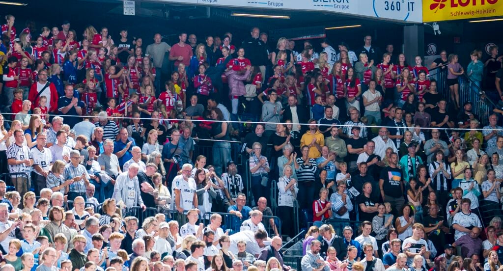 HANDBALL 2026/27: THW Kiel - Pick Szeged Eine große Menge von Fußballfans, von denen einige rote, andere weiße oder schwarze Trikots tragen, jubelt und verfolgt ein Spiel in einem Stadion, über dem Transparente zu sehen sind.
