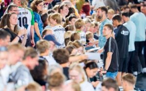 Eine gut besuchte Veranstaltung in einem Innenraum mit vielen Kindern und Erwachsenen, von denen einige Sporttrikots tragen, miteinander interagieren und in einer Schlange warten – möglicherweise auf Autogramme oder Fotos. Die Atmosphäre ist lebhaft und geschäftig.