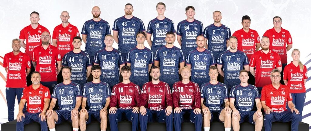 26_vor_SG_Mannschaftsbild-2627-45x29cm_12082026 Eine Herren-Handballmannschaft posiert in blauen und roten Trikots für ein Gruppenfoto. Vier Reihen aus Spielern und Betreuer stehen und sitzen vor einem hellen Hintergrund.