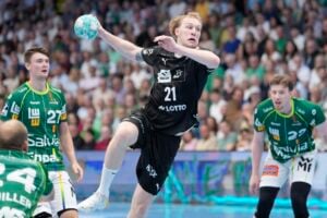 Ein Handballspieler in schwarzer Spielkleidung springt hoch, um den Ball zu werfen, während drei Gegner in grüner Spielkleidung zuschauen. Im Hintergrund ist eine Zuschauermenge in einem Stadion zu sehen.