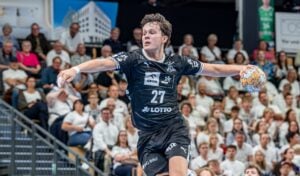Ein Handballspieler in schwarzer Spielkleidung macht sich während eines Spiels bereit, den Ball zu werfen, während im Hintergrund eine Menge Zuschauer zuschaut.