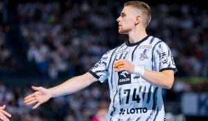 Ein männlicher Handballspieler in einem schwarz-weißen Trikot streckt während eines Spiels die Hand zum Handschlag aus, im Hintergrund ist eine verschwommene Menschenmenge zu sehen, als der THW Kiel in der Handball-Bundesliga beim ThSV Eisenach antritt.