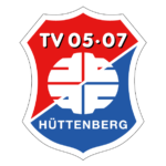 Das schildförmige Logo ist diagonal geteilt; oben links ist es rot mit weißem Schriftzug „TV 05.07“ und unten rechts blau mit der Aufschrift „HÜTTENBERG“. In der Mitte befindet sich ein weißes abstraktes Motiv, das sich über beide Farbfelder erstreckt.