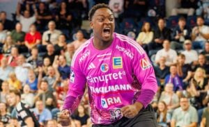 Ein Handballtorwart in einem knallpinken Trikot jubelt vor einer vollbesetzten Halle.