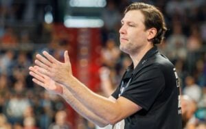 Ein Mann in einem schwarzen Polohemd, der am Spielfeldrand einer Sportveranstaltung klatscht.
