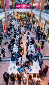 Eine Aufnahme aus der Vogelperspektive eines überfüllten Gangs in einem Einkaufszentrum, in dem eine Autogrammstunde stattfindet, bei der die Menschen an langen Tischen Schlange stehen, um Sportler zu treffen.