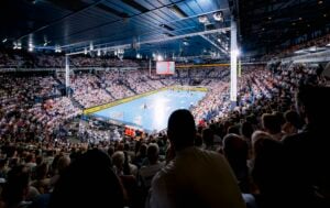 Eine vollbesetzte Halle während eines Handballspiels, von den Zuschauerrängen aus gesehen.
