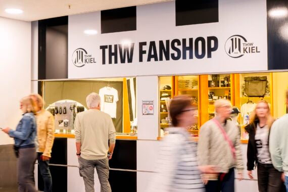 Einkäufer gehen am Fanshop des THW Kiel vorbei, in dessen Schaufenster Mannschaftskleidung und Fanartikel ausgestellt sind.