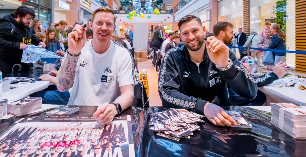 HANDBALL 2026/27: THW Kiel bei Autogrammstunde im CITTI Park Zwei Handballspieler des THW Kiel signieren während einer Autogrammstunde im CITTI Park Kiel Plakate für Fans.