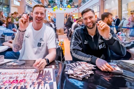 Zwei Handballspieler des THW Kiel signieren während einer Autogrammstunde im CITTI Park Kiel Plakate für Fans.